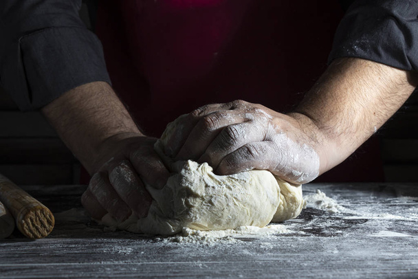 Man's hands knead the dough. Close-up. Dark background - Photo, Image