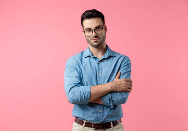 sexy young guy wearing glasses and crossing arms, standing on pink background - Photo, Image
