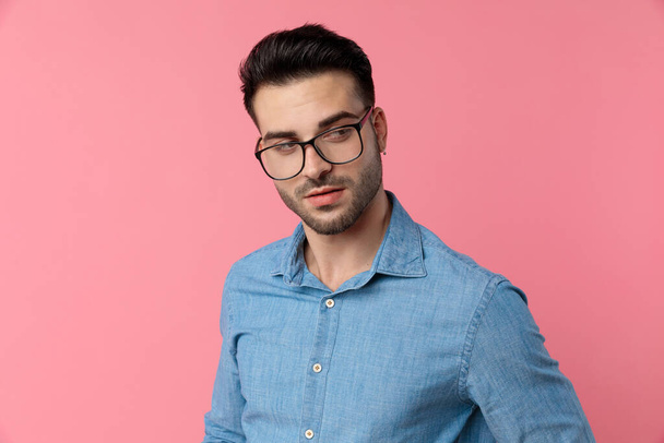 sexy módní chlap nosí brýle a hledá na straně na růžovém pozadí - Fotografie, Obrázek