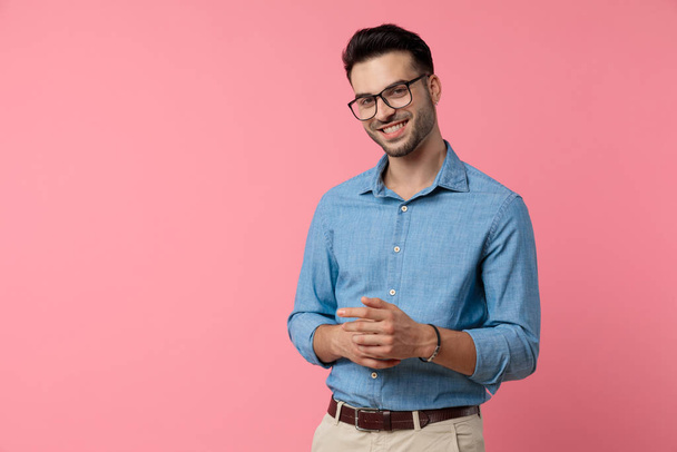 glücklicher junger Mann lächelt und berührt Hände auf rosa Hintergrund - Foto, Bild