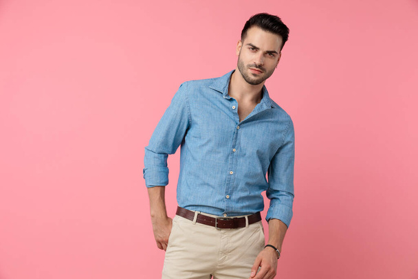 young casual model wearing denim shirt, holding hands in a fashion pose and standing on pink background - Photo, Image