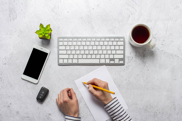 hands on the keyboard, car keys, cup of coffee, blank sheet of paper, a pencil and a room flower on a concrete background. Banner. Concept car purchase, work, business, freelance. Top view, flat lay. - Photo, Image
