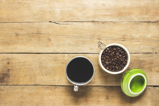 Tasse mit frischem Kaffee und einer Dose mit Kaffeekörnern auf einem Holztisch. Banner. Kaffee-Konzept, Plantage, Verarbeitung, Sammlung. Draufsicht, flache Lage. - Foto, Bild