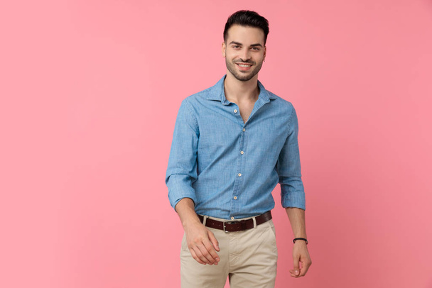 щасливий молодий чоловік в джинсовій сорочці посміхається і ходить на рожевому фоні
 - Фото, зображення