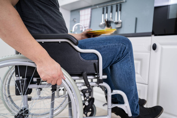 Handicapped Man Sitting On Wheelchair In Kitchen Holding Dishes - Zdjęcie, obraz