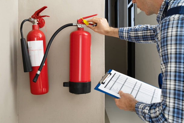 Male Professional Checking The Condition Of A Fire Extinguisher  - 写真・画像