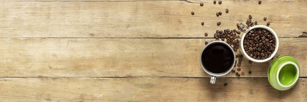 Tasse mit frischem Kaffee und einer Dose mit Kaffeekörnern, Kaffeebohnen liegen auf einem Holztisch verstreut. Banner. Kaffee-Konzept, Plantage, Verarbeitung, Sammlung. Draufsicht, flache Lage. - Foto, Bild