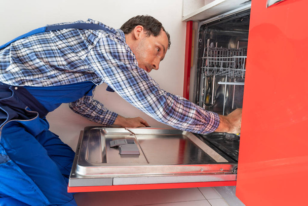 Photo Of Repairman Examining Dishwasher In Kitchen  - Foto, imagen