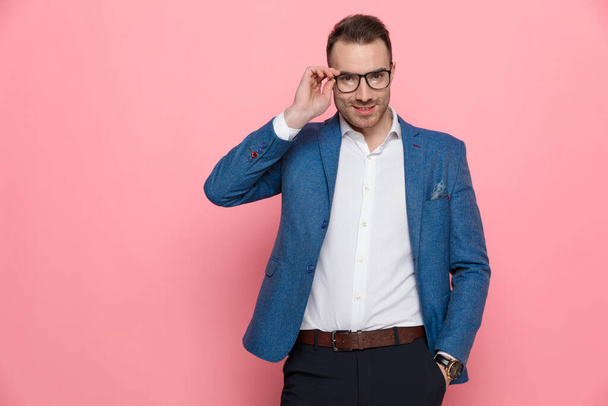 Happy fiksu rento mies riisuu silmälasit kätensä taskussaan, kun yllään seisoo vaaleanpunainen studio tausta
 - Valokuva, kuva