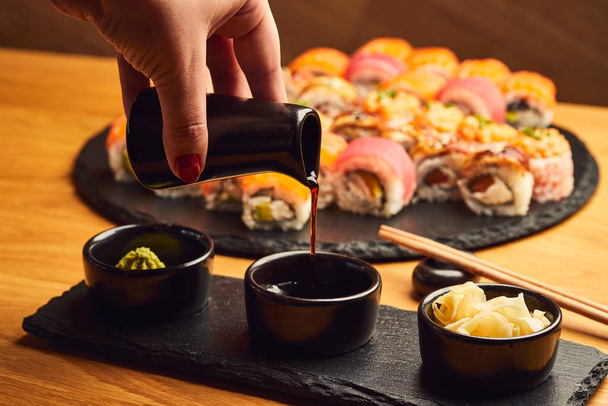 Ruční nalévání sójová omáčka (Shoyu) z malého džbánu do misky před jíst japonské jídlo, jako je sushi roll - Fotografie, Obrázek