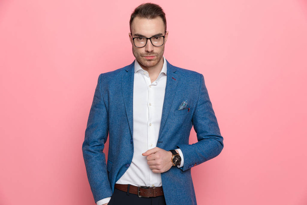 Confiante homem casual inteligente ajustando sua jaqueta e olhando para a frente, enquanto em pé no fundo do estúdio rosa
 - Foto, Imagem