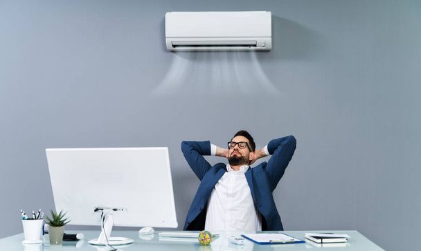 Расслабленный бизнесмен наслаждается охлаждением кондиционера в офисе
 - Фото, изображение