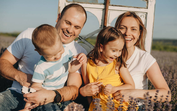 Mooie familie lachend terwijl ze hun kinderen in een lavendelveld houden tijdens een zonnige zomerdag - Foto, afbeelding