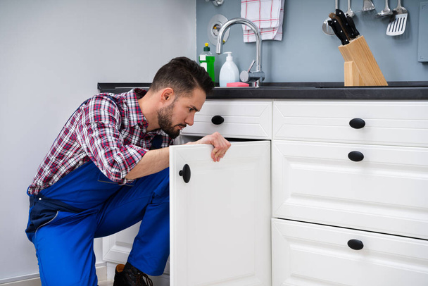 Young Handyman Fixing Sink Door In Kitchen - 写真・画像