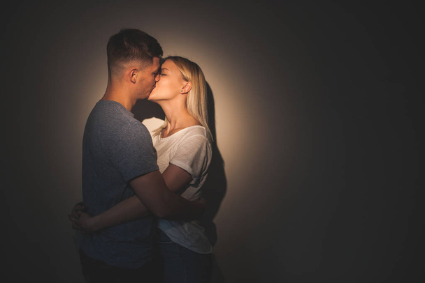 Two caucasian lovers kissing each other with a wall on background against a charming light - Photo, Image