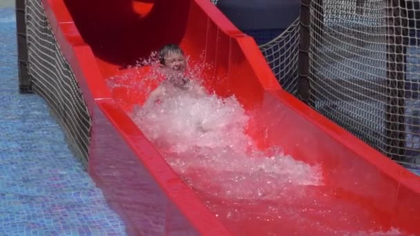 Jongensglijbaan op glijbaan in waterpark op zomervakantie. Gelukkige jongen glijdt van de glijbaan. Slow motion 240 fps - Video