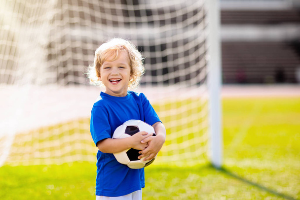 Kids play football on outdoor stadium field. Children score a goal during soccer game. Little boy kicking ball. School sports club. Training for young player. - Photo, image