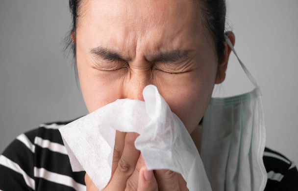 Asian young woman blowing nose in a tissue feel sick at outdoor from polluted air. Nosebleed women. Concepts of air pollution, dust allergies and health care. - Photo, Image