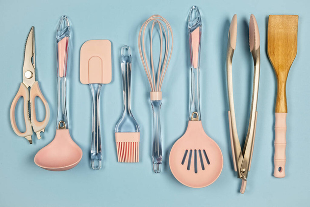 Mezcla de utensilios de cocina de metal y silicona en color rosa sobre fondo azul, vista superior
  - Foto, imagen