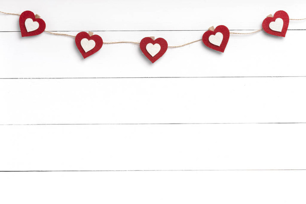 Clothespins with red hearts hanging on string behind white wooden surface. - Photo, Image