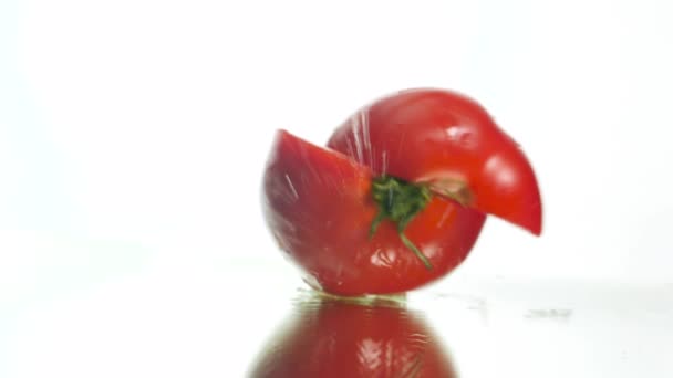 Closeup slow motion video of fresh red tomato falling on wet reflective surface and splitting in two slices. Concept of healthy nutrition and organic food. Perfect background for vegetarian or vegan - Záběry, video