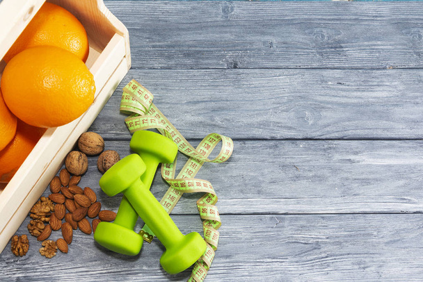 Lots of oranges, dumbbells, measuring tape on a wooden textured background. Fitness, sports nutrition - Photo, Image