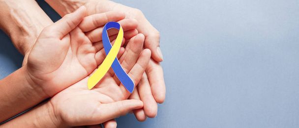 Erwachsene und Kinder halten blaue und gelbe Papierbänder in Händen, Down-Syndrom-Bewusstsein, Welt-Down-Syndrom-Tag - Foto, Bild