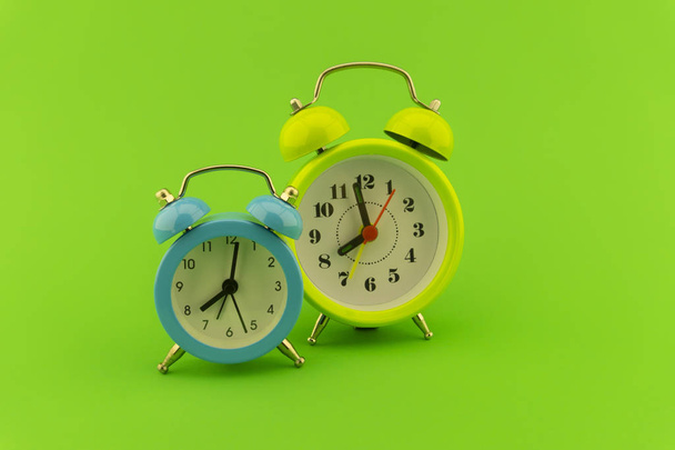 Синий и желтый двойной колокол аналоговый будильник часы на красочном зеленом фоне с копировальным пространством
 - Фото, изображение