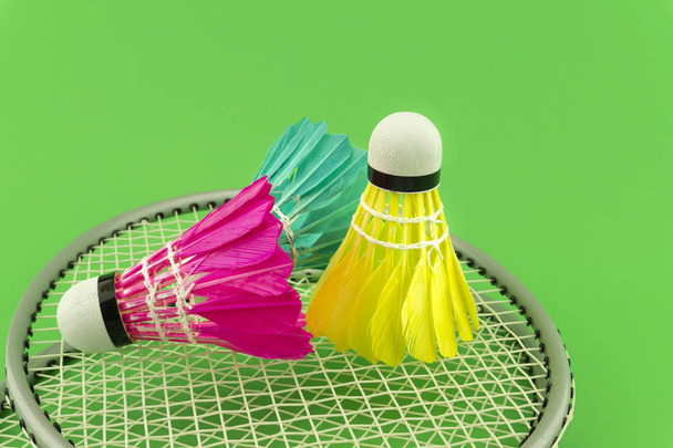 Rakiety do badmintona i kolorowe wpierane lotki w kolorze niebieskim, żółtym i różowym na zielonym tle w widoku z bliska - Zdjęcie, obraz