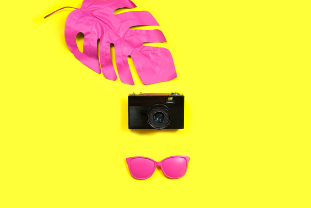 Ροζ τροπικό φύλλο παλάμης από monstera, γυαλιά ηλίου και κάμερα σε κίτρινο φόντο. έννοια της μόδας. μινιμαλισμός. Καλοκαιρινή ιδέα Αντίληψη τέχνης. Επίπεδο lay, πάνω όψη, αντιγραφή χώρου - Φωτογραφία, εικόνα