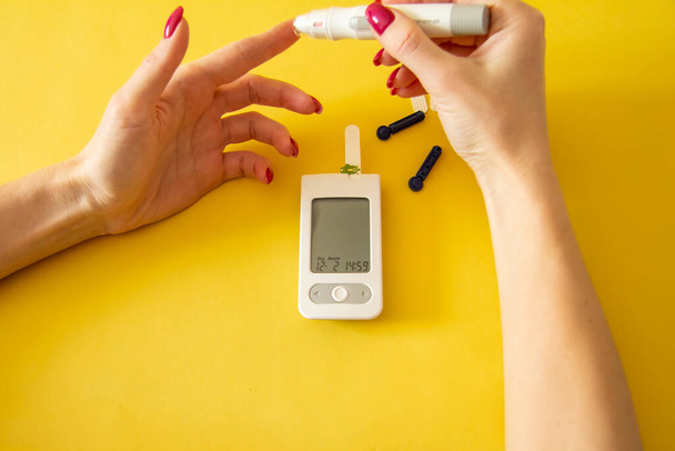 糖尿病。医療機器。医学的概念。血糖値を確認するために、指の上にランセットを使用して黄色の背景に女性の手の閉鎖血糖値計  - 写真・画像