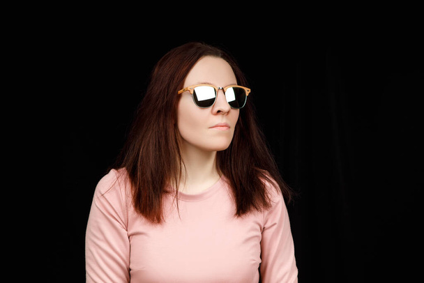 Image of sweet confident young lady standing over black background in studio, wearing pink blouse and fashionable eyeglasses, having long brown hair - Φωτογραφία, εικόνα