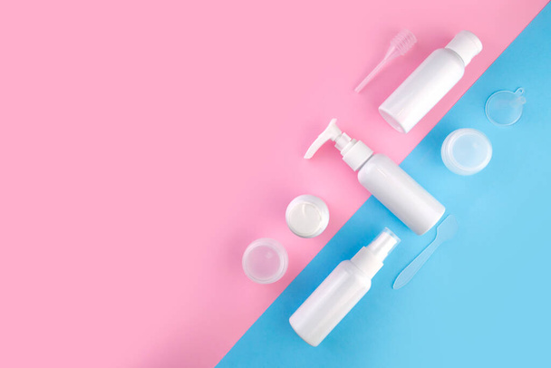 Travel size cosmetic flat lay. Top view beauty composition on pink and blue background. Cream sample bottle vacation airplane kit - Foto, Imagem