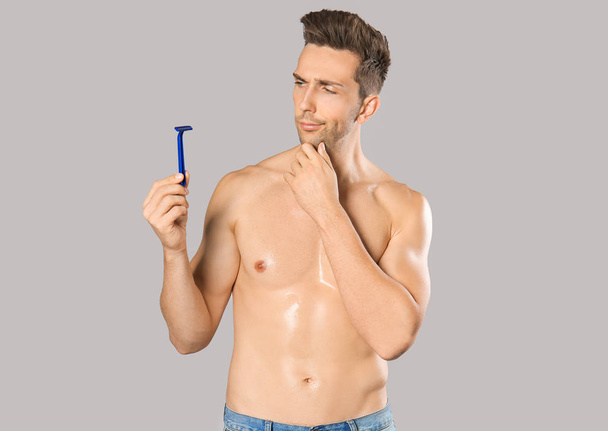 Thoughtful young man with razor on grey background - Photo, image