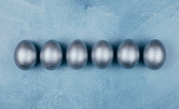 銀色の灰色のイースターの卵は、質感のある青の背景に連続しています。スペースのコピー. - 写真・画像