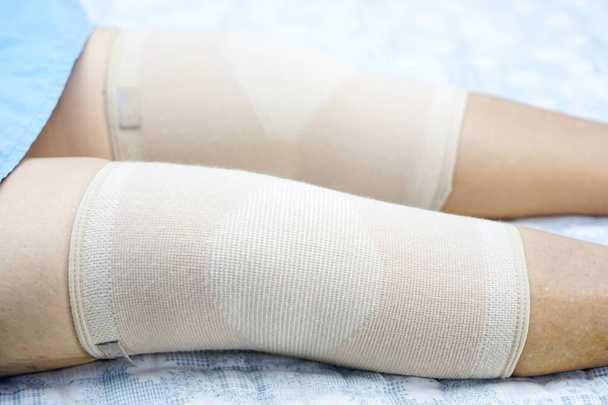 包帯圧縮膝ブレースを持つアジアの高齢女性高齢者の高齢者は、病棟のベッドの上で負傷をサポートします:健康的な強力な医療の概念  - 写真・画像