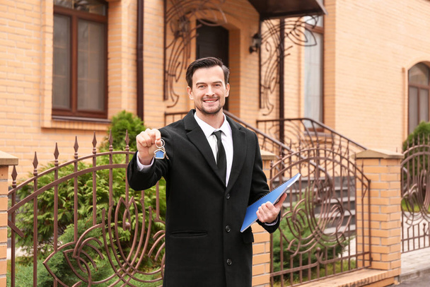 Agente inmobiliario masculino con llave cerca de casa para la venta al aire libre
 - Foto, imagen