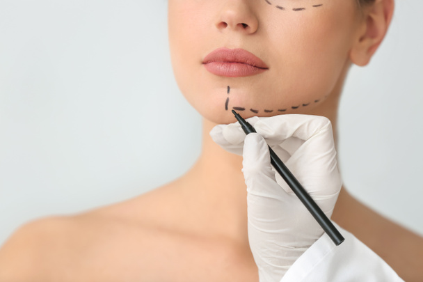 Plastic surgeon applying marking on female face against light background - Foto, imagen