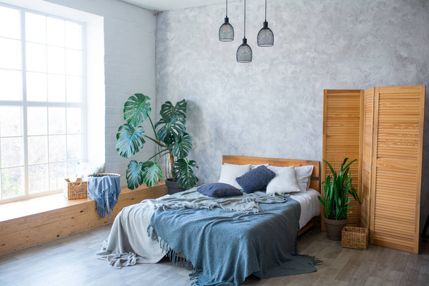 Przytulna sypialnia w luksusowym apartamencie typu studio z bezpłatnym układem w stylu poddasza z dużym oknem panoramicznym i zieloną rośliną. - Zdjęcie, obraz