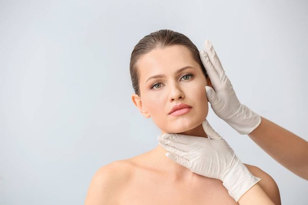 Chirurg plastyczny dotykający twarzy młodej kobiety na jasnym tle - Zdjęcie, obraz