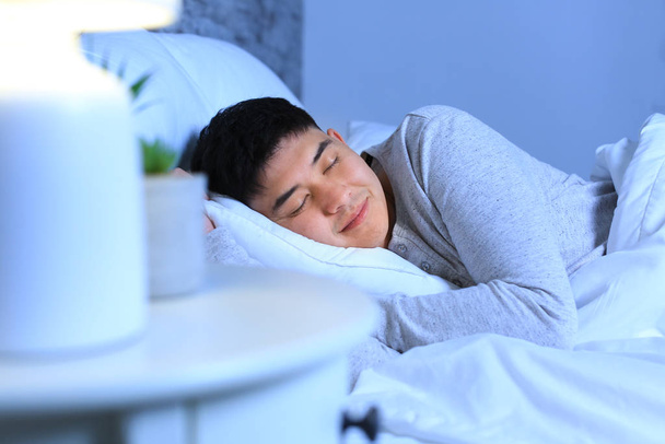 アジア人男性は夜にベッドで寝て - 写真・画像