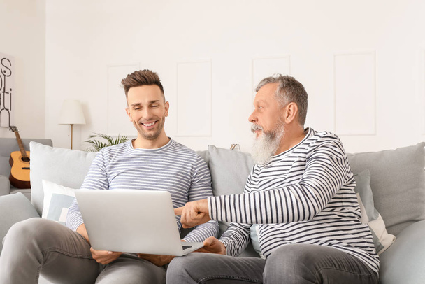 Hombre mayor y su hijo adulto usando el portátil en casa
 - Foto, Imagen
