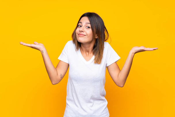 Young woman over isolated yellow background making doubts gesture - Foto, Bild
