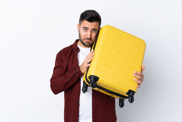 Młody przystojny mężczyzna na odizolowanym białym tle na wakacjach z walizką podróżną i nieszczęśliwy - Zdjęcie, obraz