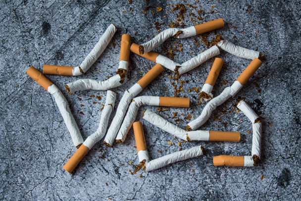 A pile of broken cigarettes on a gray textural background. The concept of a healthy lifestyle, quitting Smoking - Fotoğraf, Görsel