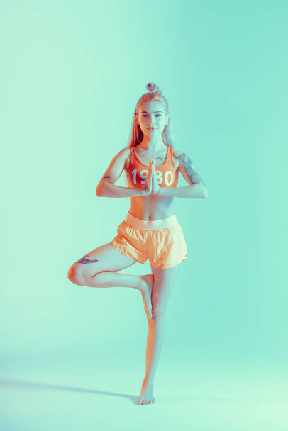 Jovem atlética fazendo exercício de ioga. Vestida de fato desportivo retrô. Luzes de néon. Luz específica do estúdio
 - Foto, Imagem