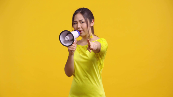 displeased asian girl screaming and holding megaphone isolated on yellow  - Footage, Video