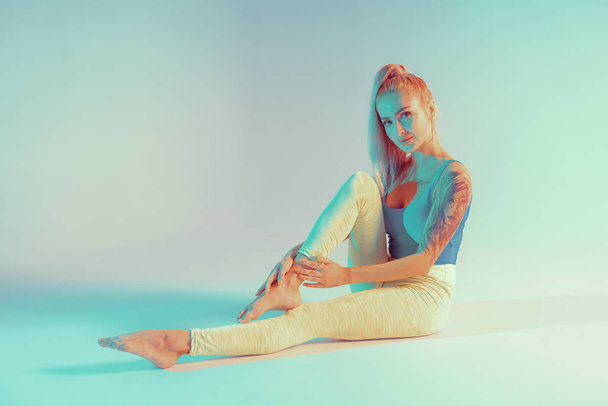 Athletic young woman doing yoga exercise. Dressed in retro sportswear. Neon lights. Specific studio light - Photo, Image