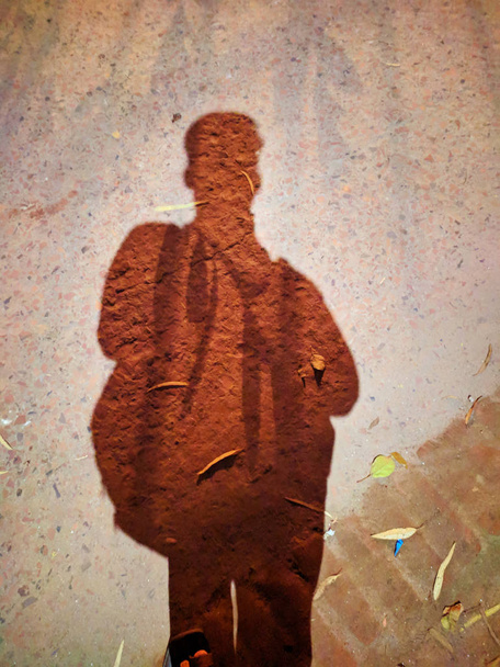 Schatten eines Schuljungen, der mit einer Tasche in der City Street steht. Schatten eines Mannes auf Straßenbeton Hintergrund. Dunkler Schatten auf der Straße des Landes. Schatten eines jungen Mannes. - Foto, Bild