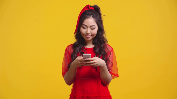 glücklich asiatische Mädchen SMS auf Smartphone isoliert auf gelb  - Filmmaterial, Video